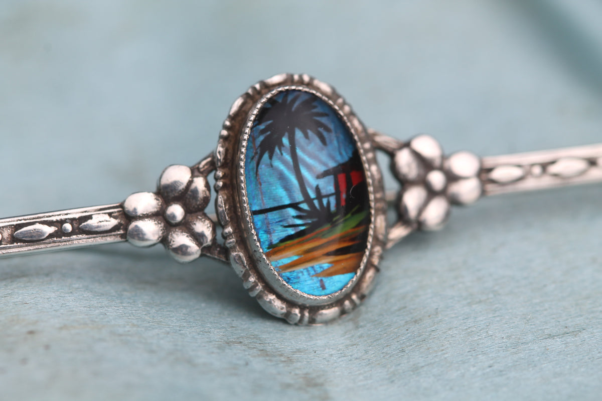 Close-up of butterfly wing brooch showing tropical palm tree scene