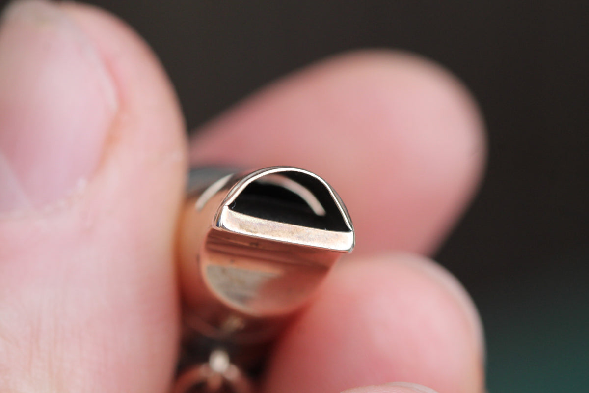 Side view of antique gold whistle showing mouthpiece and circular base