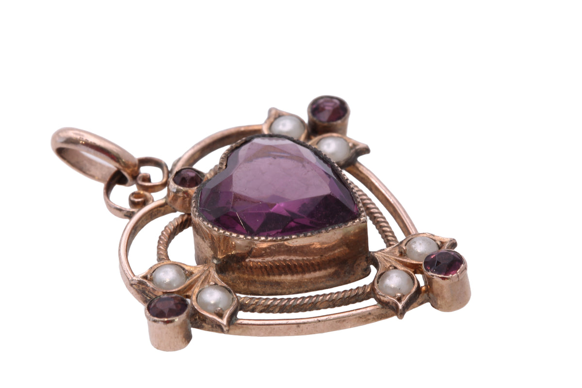 Antique heart pendant held in hand showing seed pearls and purple paste stones