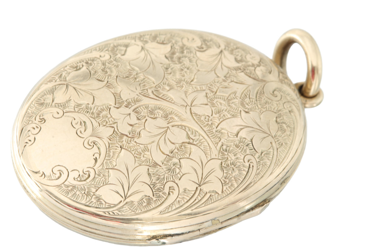 Antique enamel locket held in hand showing engraved border